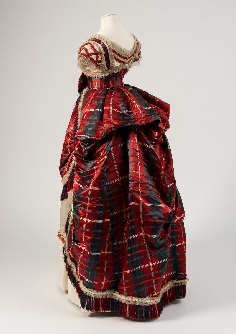Image: A back view of a red, green and cream silk satin evening dress from 1870