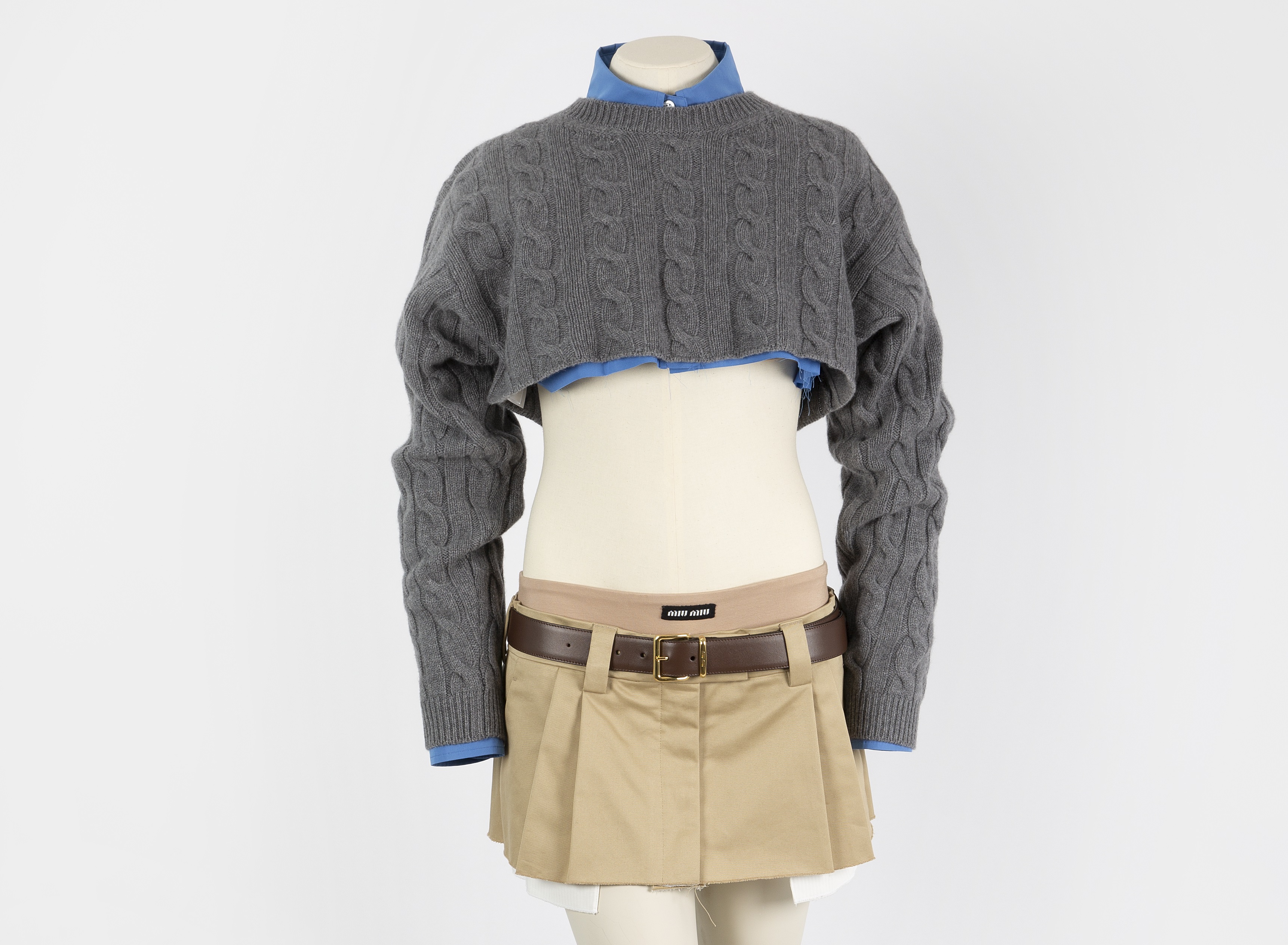 Image: A micro miniskirt paired with a scissored blue cotton shirt and a cropped grey cable knit cashmere sweater. 