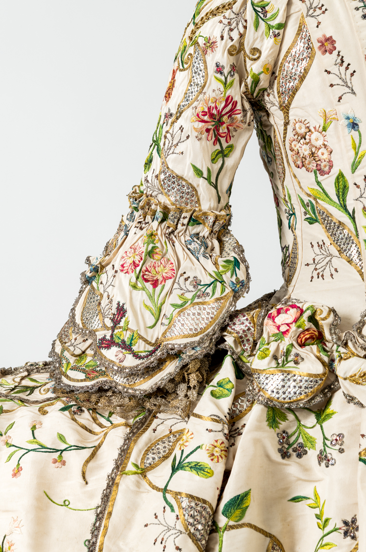 A close up of an 18th Century gown showing detailed embroidery of plants and flowers