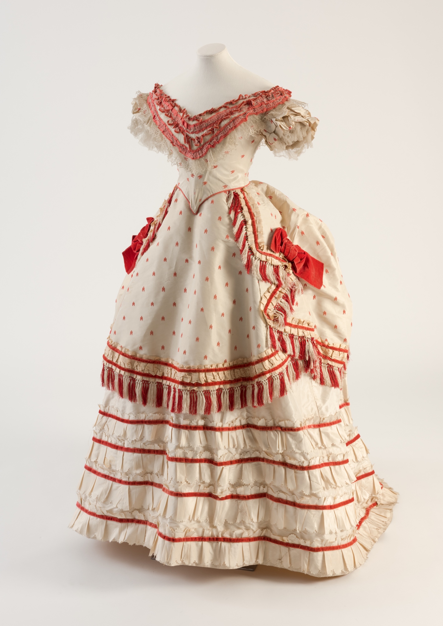 A white 1870s gown with lots of red accents, frills and bows