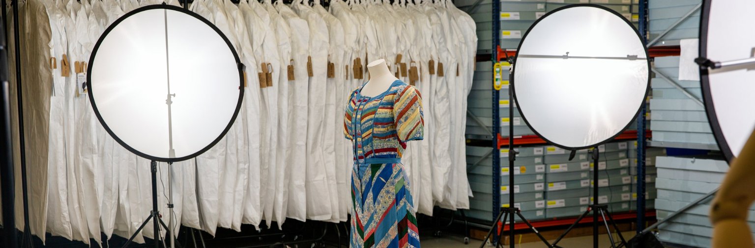 A photograph of the collections store with a dress from the collection in the centre and photography equipment surrounding it. The dress is being photographed