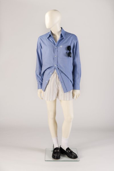 Light blue cotton shirt, striped boxer-style shorts worn with white crew socks, classic black Horsebit loafers, and sunglasses. S/S 25